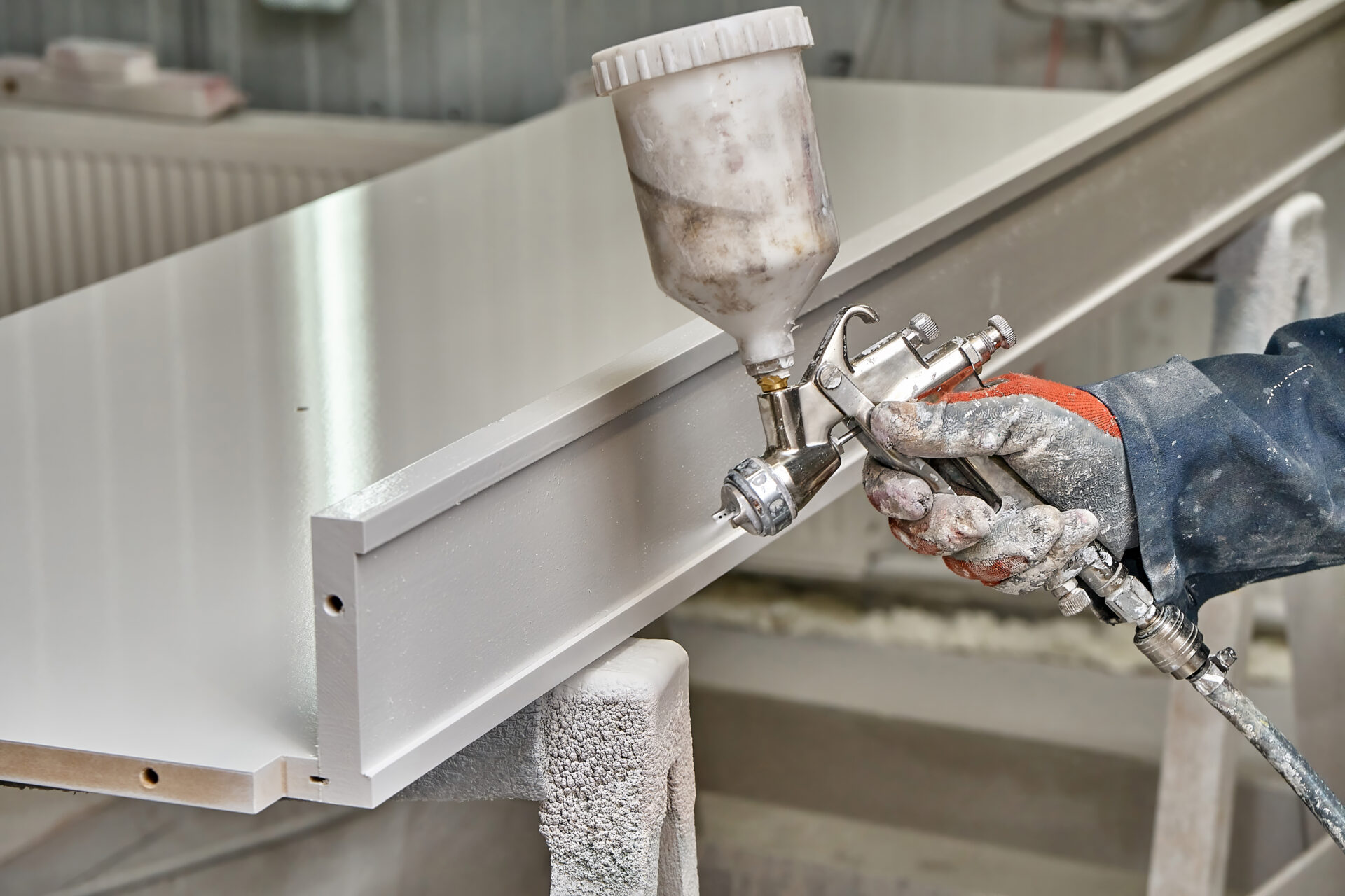 Man painting furniture details in a spray booth. worker using spray gun. furniture manufacture